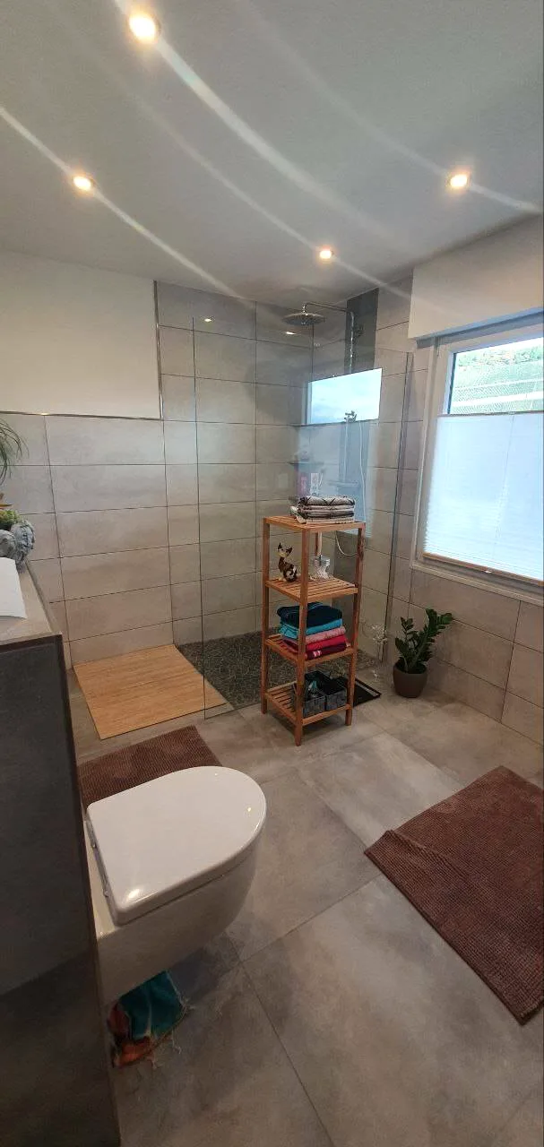 Bad mit Dusche, Hänge-WC, Handtuchheizkörper und grauen Bodenfliesen