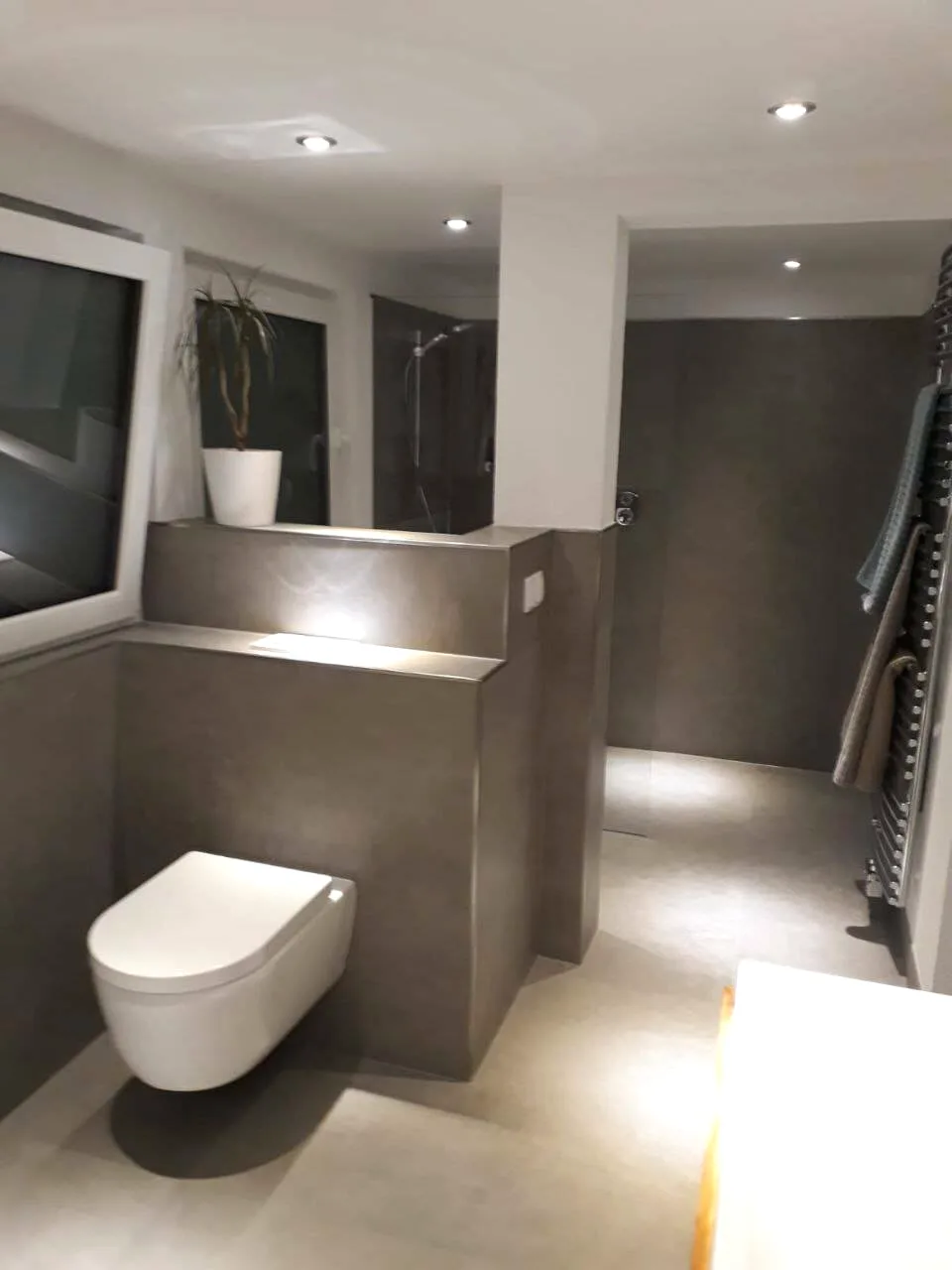Bad in Grau mit gefliester Vorwand, Hänge-WC und Spots in der Decke