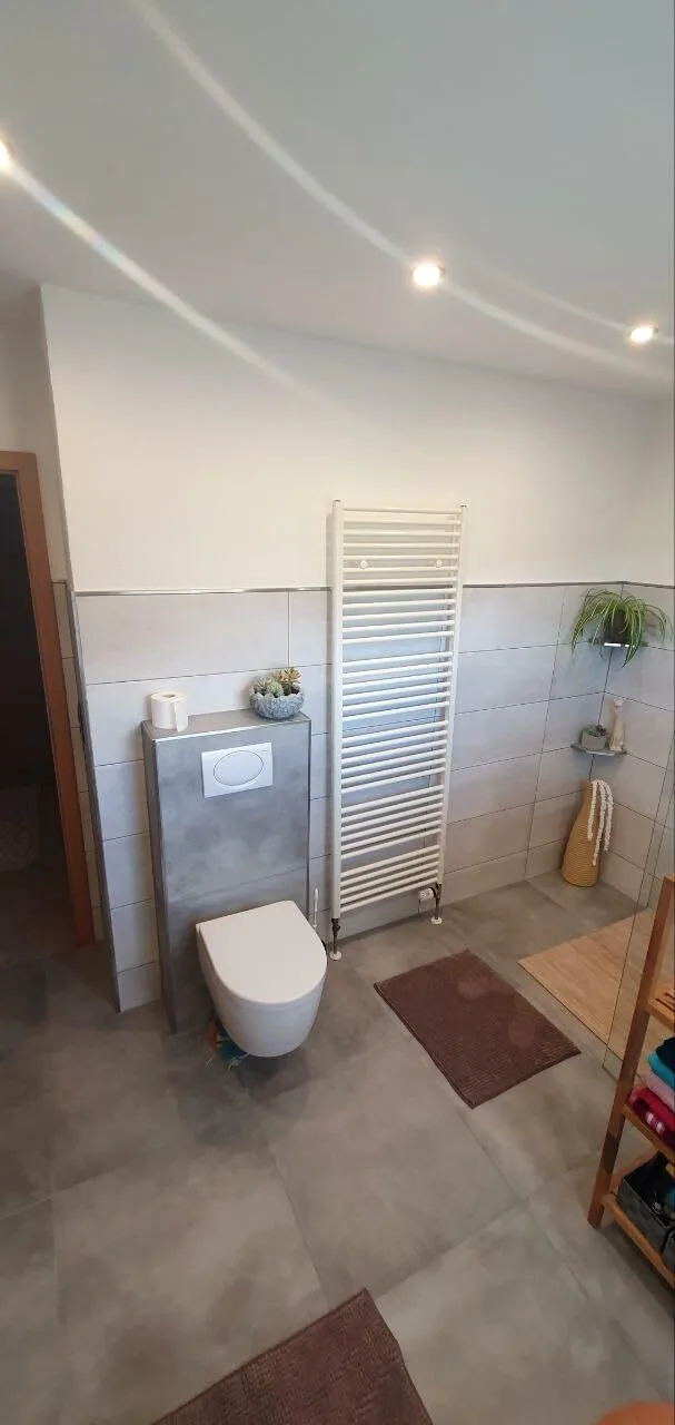 Bad mit Hänge-WC, weißem Handtuchheizkörper und grauem Fliesenboden