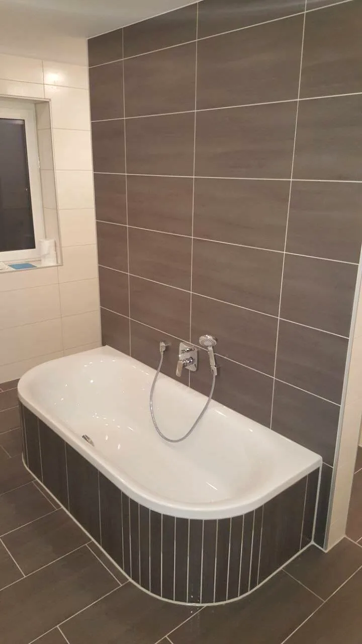 Badewanne mit Verkleidung vor braunen Wandfliesen im Streifendesign
