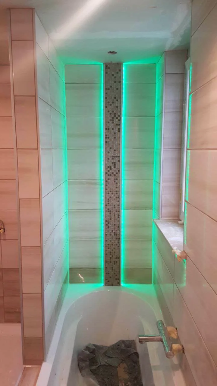 Badewanne in einer gefliesten Nische mit grüner LED-Beleuchtung und Mosaikband