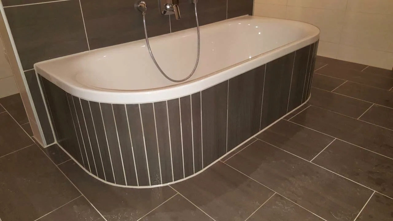 Gerundete Badewannenverkleidung mit grauen Streifenfliesen und Bodenfliesen in Grau