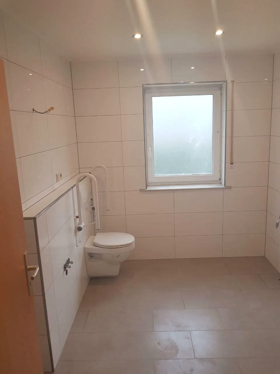 Barrierefreies WC mit Fenster, Haltegriff und hellen Wandfliesen