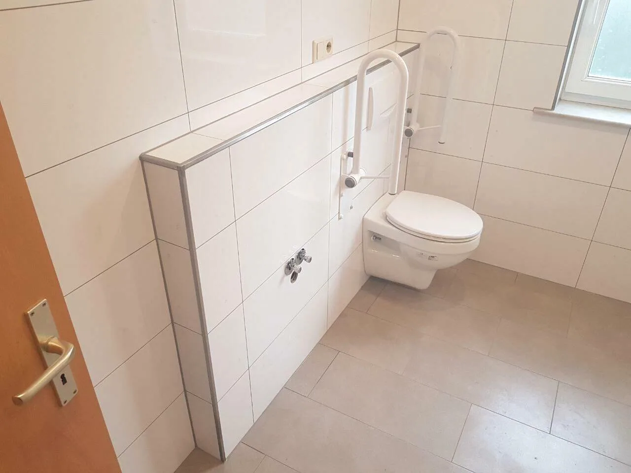 Barrierefreies WC mit Haltegriffen, weißen Wandfliesen und beigem Boden