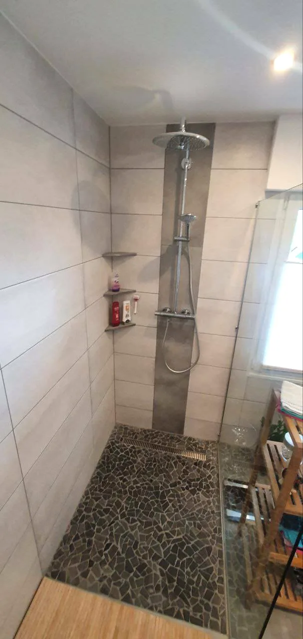 Dusche mit Kieselsteinboden, Glaswand und Holzboden davor