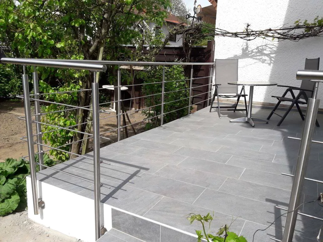 Terrasse mit grauen Feinsteinzeugplatten und Edelstahlgeländer im Garten
