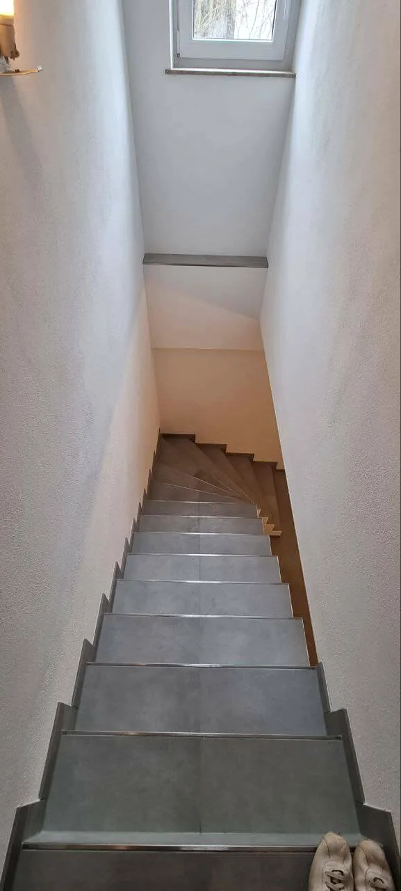 Gerade Treppe mit grauen Fliesen und Fenster am Treppenabsatz